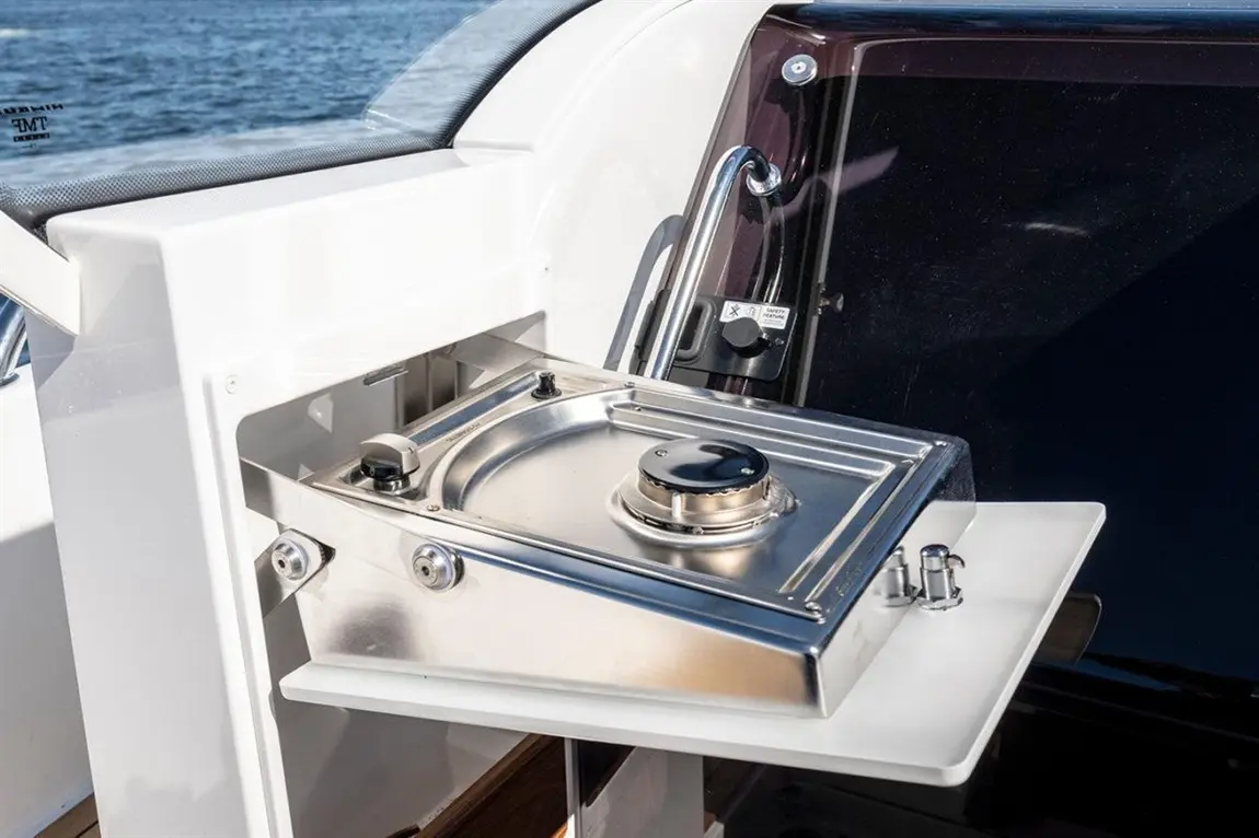 Stainless steel cooking stove on a boat’s outdoor galley, with water in the background and safety features visible.
